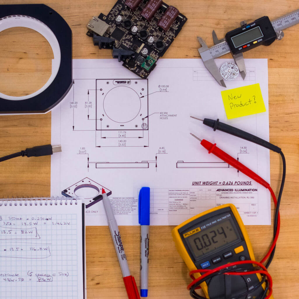 engineer's table with diagram of a light, notepad, markers, and other tools